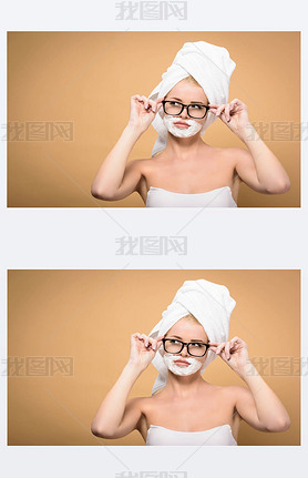 young woman with towel on head and shing cream on face adjusting eyeglasses and looking away isola