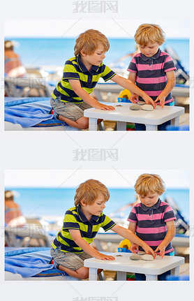 Two little kid boys playing on beach with stones