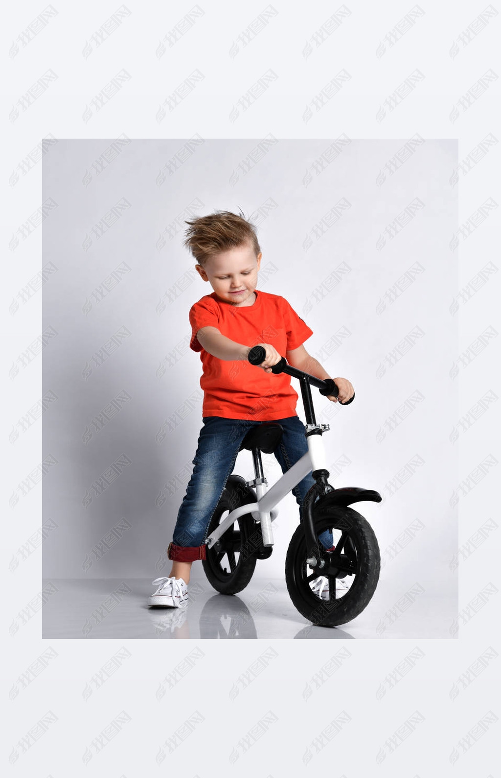 Young kid boy in orange t-shirt and blue jeans biker sits on his bicycle and looks at it like check 