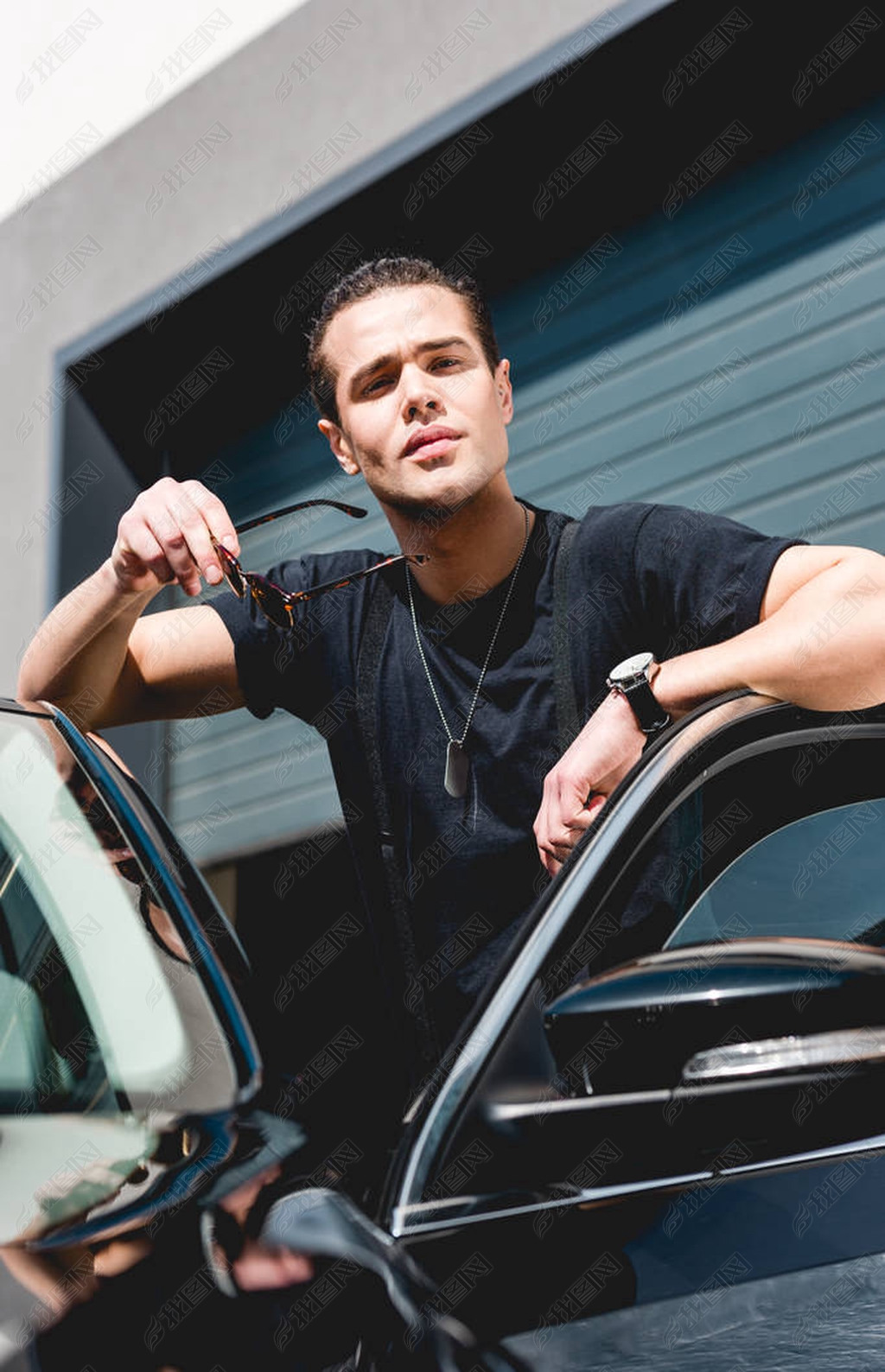 原创英俊的时尚男子靠在汽车上并在车库附近摆姿势版权可商用