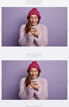 Happy female blogger uses modern gadget for browsing internet, mobile phone application, gazes with 