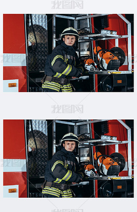 portrait of firefighter in helmet standing at truck at fire station