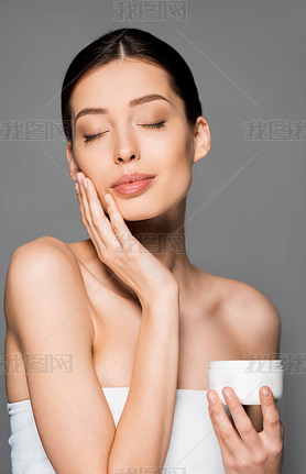 beautiful tender girl with closed eyes applying face cream, isolated on grey