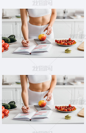 Cropped view of fit sportswoman writing calories while weighing apple on kitchen table, calorie coun