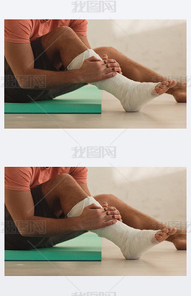 Cropped view of man holding broken leg and sitting on fitness mat on floor