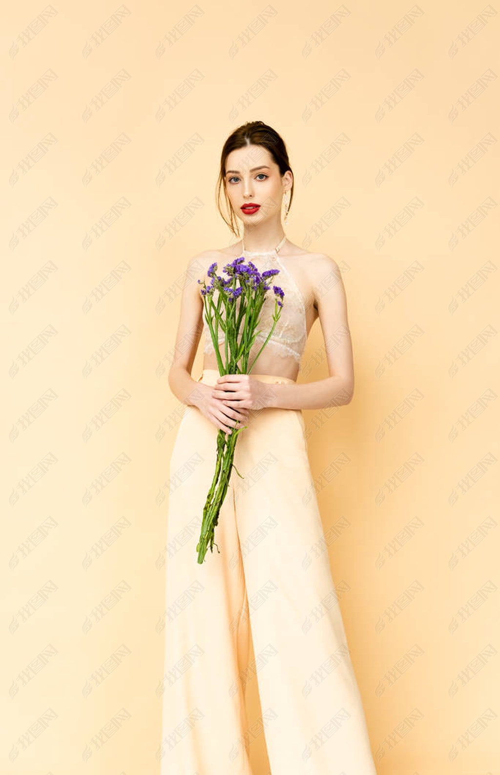 attractive woman holding purple limonium flowers and standing isolated on beige 