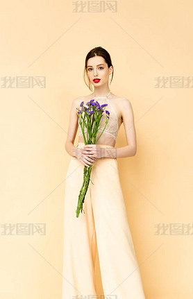 attractive woman holding purple limonium flowers and standing isolated on beige 