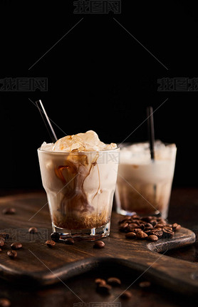 white russian cocktail in glasses with straws on wooden board with coffee grains isolated on black