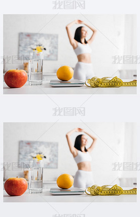 Selective focus of measuring tape, fruits with scales and glass of water on table and sportswoman in