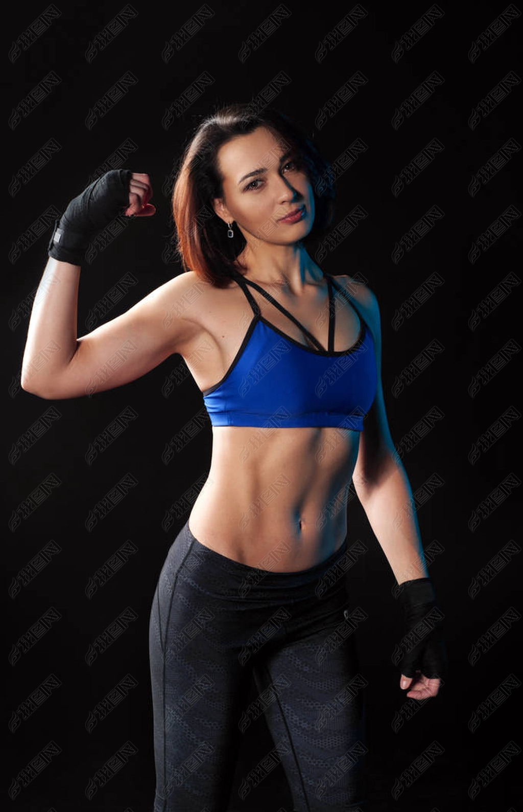 Beautiful young female athlete in blue sports top and leggings shows bitsipts. Black background. The