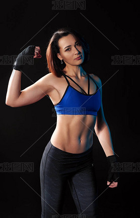 Beautiful young female athlete in blue sports top and leggings shows bitsipts. Black background. The