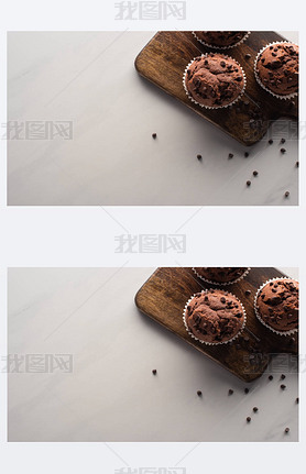 top view of fresh chocolate muffins on wooden cutting board on marble surface