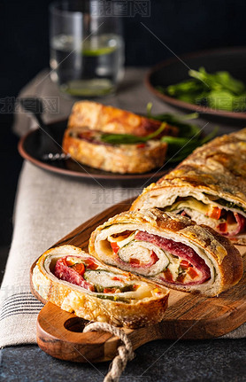 Traditional Italian Stromboli stuffed with cheese, salami, red pepper and spinach. Photo in a dark s