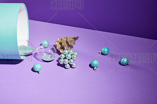 Christmas decoration and hourglass scattered from blue gift box on purple background