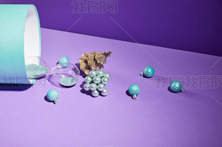 Christmas decoration and hourglass scattered from blue gift box on purple background