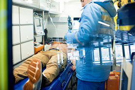 Young paramedic in uniform standing by stretcher with sick shirtless man while giving him first aid 