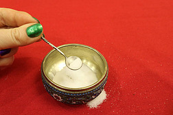 在红色桌布上撒盐的银制盐瓶上，有一个小的古董银勺子，妇女的手指上有盐. 