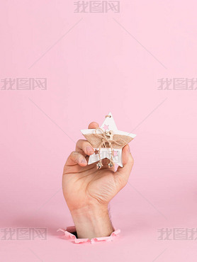 A male hand sticks out of a hole in pink paper, holds a Christmas tree ornament. Christmas concept s