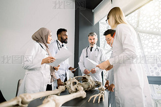 Team of young diverse doctors, students, scientists in white labcoats having discussion on the meeti