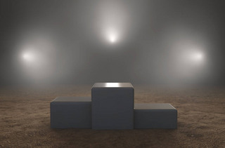 An empty classic winners podium on sand backlit by dramatic spot lights on a dark moody background -