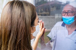 Sad woman communicating with her sick father through a window while visiting in isolation room