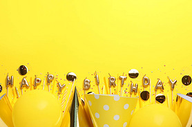 Phrase Happy Birthday of candles and party decor on yellow background, flat lay. Space for text