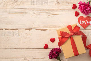 Kraft gift box with red ribbon bow and carnation, concept of giving present at mother's day as surpr