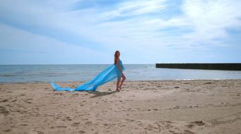 Romanticphotosessiononbeach.Pregnantcouplewithbluefabricinwind