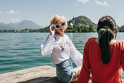 美丽的女孩在太阳镜看照相机, 当坐与女朋友在山湖的木码头, 流血, 斯洛文尼亚