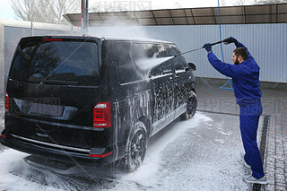 Worker cleaning automobile with high pressure water jet at car w