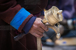 Old Tibetan man holding wooden walking stick and buddhist prayer wheel, Ladakh, India