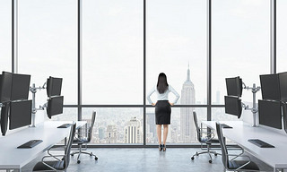 Rear view of a lady in formal suit who is looking out the window in the modern panoramic office with