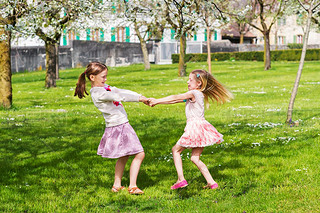 Two little girls playing in spring garden on a nice sunny warm day, wearing skirts