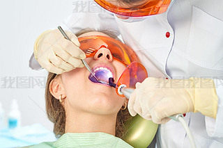 Girl child at the doctor. Dentist places a filling on a tooth with dental polymerization lamp in ora