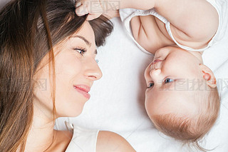 Happy mother with a baby lying on a white bed