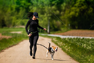Sport girl is running with a dog (Beagle) on the rural road towadrds camera.