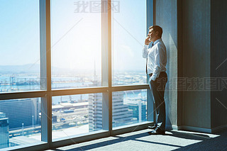 Mature and cnofident business executive looking looking out of large windows at a view of the city b