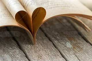 Heart shape from opened book pages on wooden background.