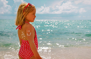 sun protection at beach- little girl with sunblock cream on shoulder