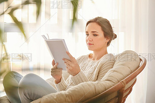 Young woman reading book on lounge chair at home