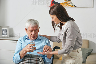 Young adult daughter giving pills to senior father while taking care of him after stroke