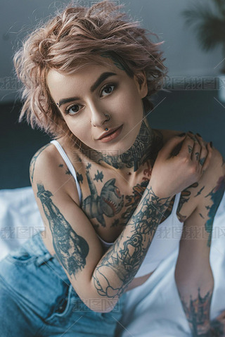 portrait of tender tattooed girl with pink hair in bedroom