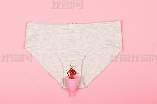 Woman panty with a menstrual cup on the pastel pink background.