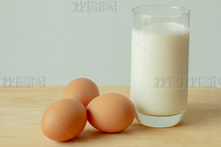 Glass of milk and eggs on white table and white background.