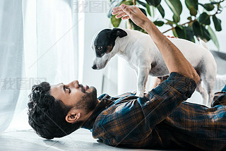 side view of iling and handsome bi-racial man holding Jack Russell Terrier