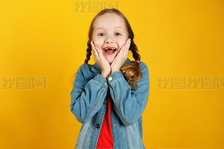 Cheerful emotional little girl in a denim shirt on a yellow background. The child is pleased with th