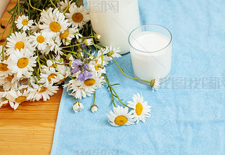 Simply stylish wooden kitchen with bottle of milk and glass on table, summer flowers camomile, healt