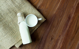 A bottle of milk and glass of fresh milk on a sack with wooden table background