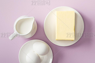 top view of butter, milk jug and boiled eggs on white plates on violet background