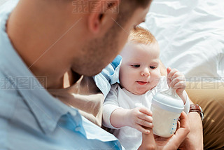 selective focus of cute baby boy touching bottle with milk in fathers hands